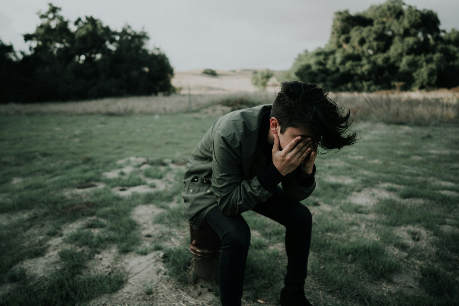 A person sitting alone, holding their face in their hands